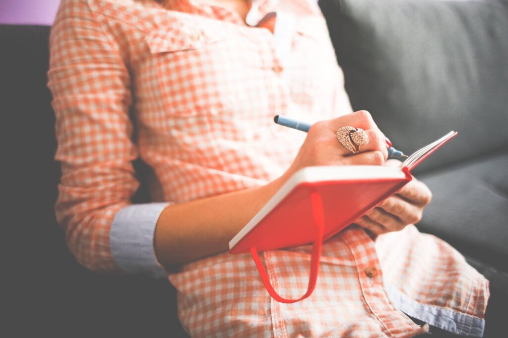 woman writing new years resolutions in red notebook